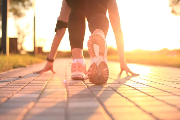Jonge fitness aantrekkelijke sportieve meisje runner in beginpositie, close-up op schoen, buiten bij zonsondergang of zonsopgang. — Stockfoto