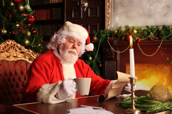Retrato de Papai Noel feliz sentado em seu quarto em casa perto da árvore de Natal e lendo carta de Natal ou lista de desejos. — Fotografia de Stock