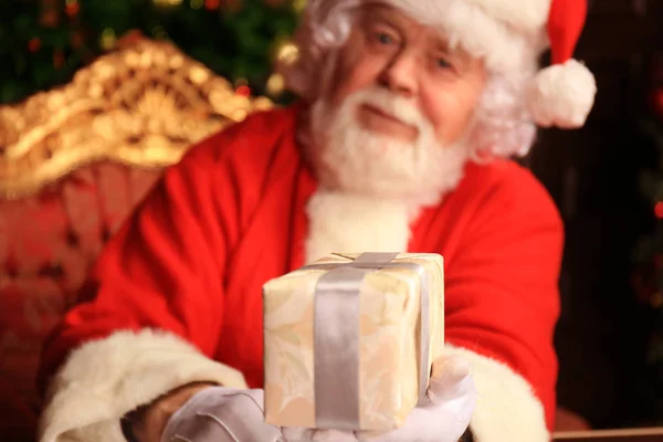 Portrait de Père Noël heureux assis dans sa chambre à la maison près de l'arbre de Noël avec boîte cadeau. — Photo