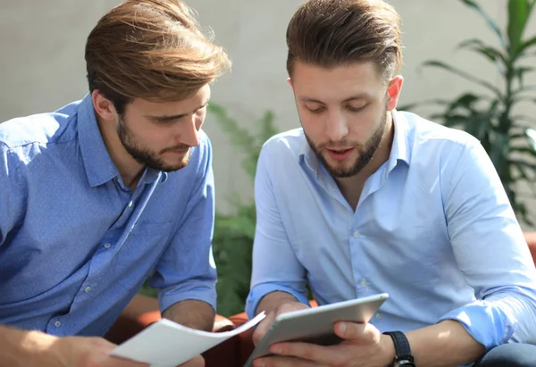 Uomo d'affari maturo che utilizza un tablet digitale per discutere informazioni con un collega più giovane in un moderno ufficio commerciale . — Foto Stock