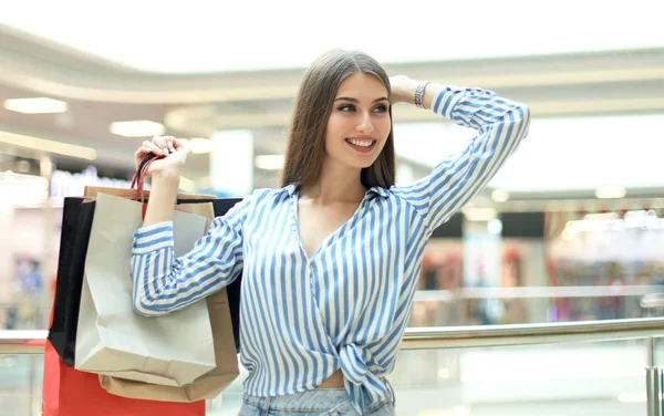 Jonge vrouw met boodschappentassen glimlachen over mall achtergrond. — Stockfoto