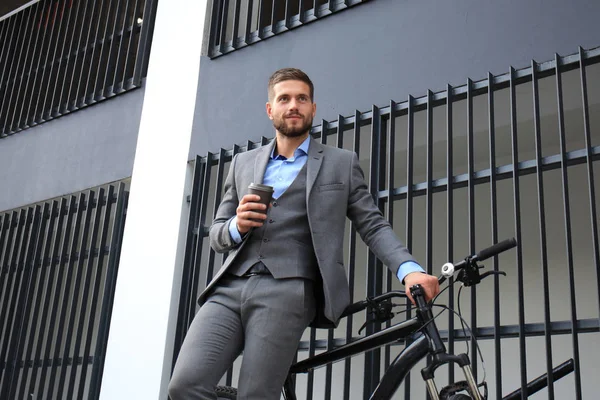 Jovem empresário confiante com sua bicicleta bebendo café ao ar livre . — Fotografia de Stock
