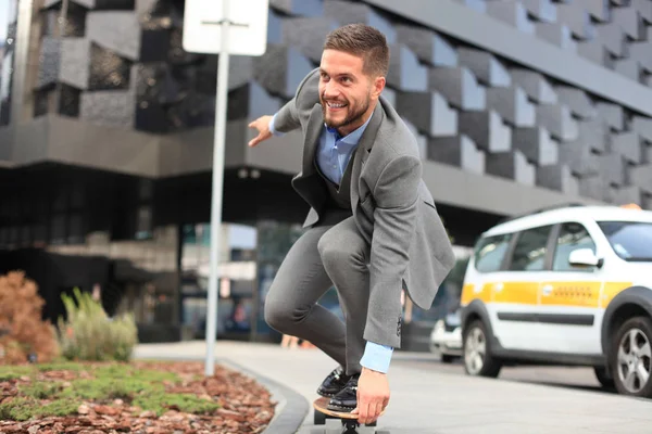 Giovane uomo d'affari sicuro in giacca e cravatta a longboard che si affretta al suo ufficio, per strada in città — Foto Stock