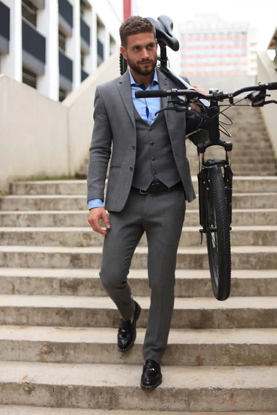 Joven empresario confiado llevando su bicicleta mientras camina al aire libre . — Foto de Stock