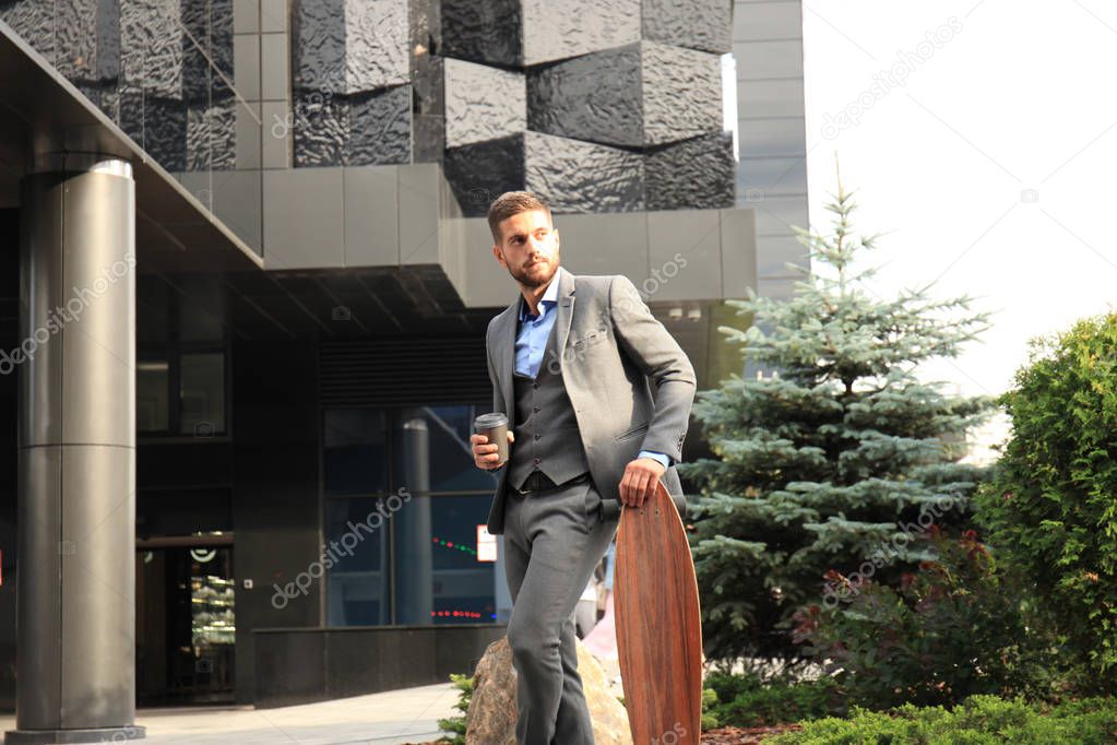 Confident young businessman walking on the street, using longboard.