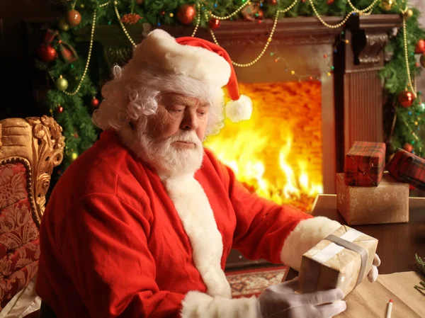 Retrato de Papai Noel feliz sentado em seu quarto em casa perto da árvore de Natal com caixa de presente. — Fotografia de Stock