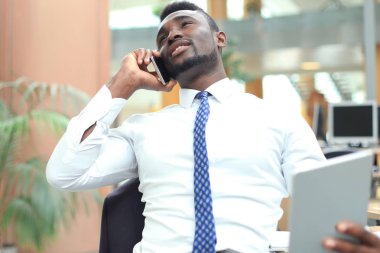 Tablet bilgisayar kullanarak ve telefonda konuşurken başarılı bir Afrikalı-Amerikalı girişimci.