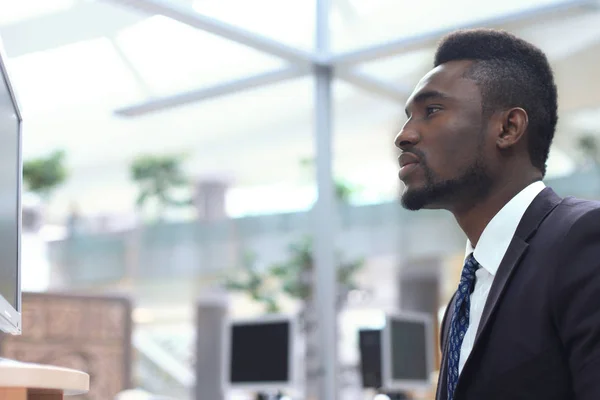 Retrato del exitoso hombre de negocios afroamericano sentado en el escritorio con computadora en la oficina . —  Fotos de Stock