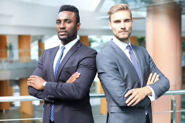 African american and caucasian business partners standing back to back together and looking in camera, in office.