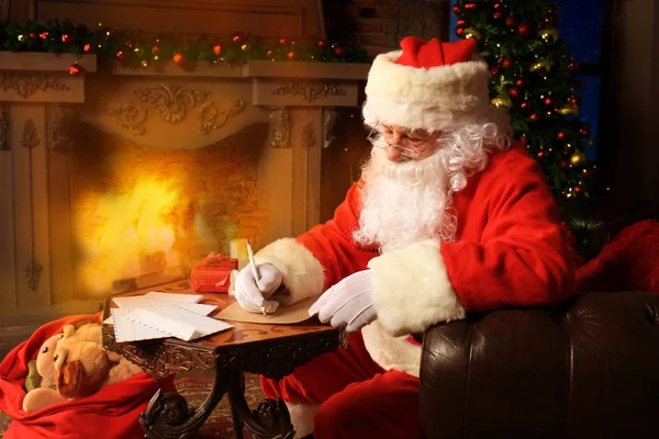 Retrato de Papai Noel feliz sentado em seu quarto em casa perto da árvore de Natal e respondendo cartas de Natal. — Fotografia de Stock