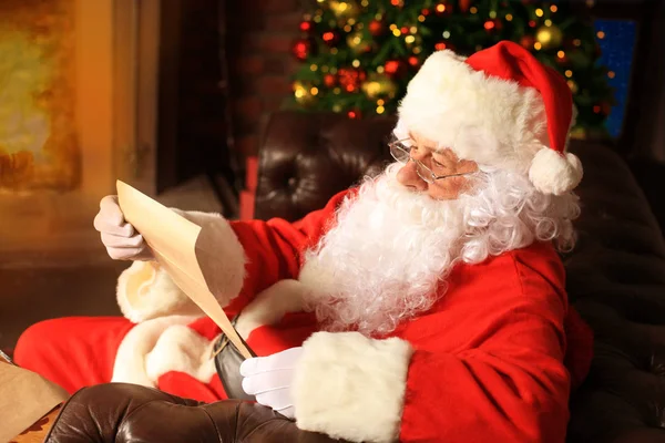 Portret szczęśliwego Mikołaja siedzącego w pokoju obok choinki i czytającego list świąteczny lub listę życzeń. — Zdjęcie stockowe