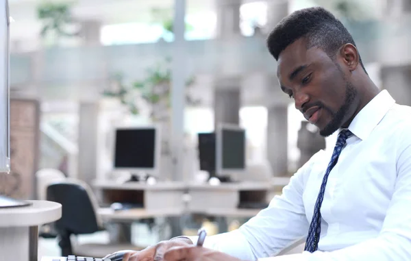 Retrato del exitoso hombre de negocios afroamericano sentado en el escritorio con computadora en la oficina . —  Fotos de Stock