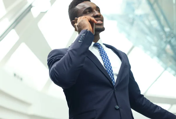 近代的なオフィスに携帯電話で話しているハンサムなアフリカ系アメリカ人ビジネスマン. — ストック写真