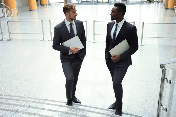 Dos jóvenes empresarios multinacionales hablando mientras escaleras en el moderno edificio de oficinas . —  Fotos de Stock