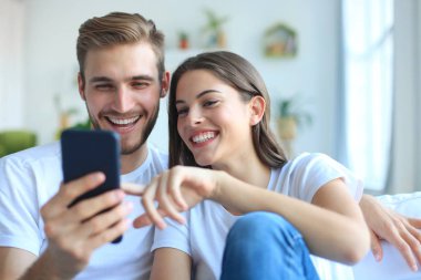 Genç çift evdeki kanepede oturmuş akıllı bir telefonla online içeriği izliyorlar..