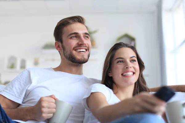 Jong liefhebbend paar op de bank thuis kijken tv en lachen. — Stockfoto