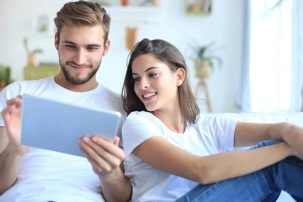 Pareja joven viendo contenido multimedia en línea en una tableta sentada en un sofá en la sala de estar. —  Fotos de Stock