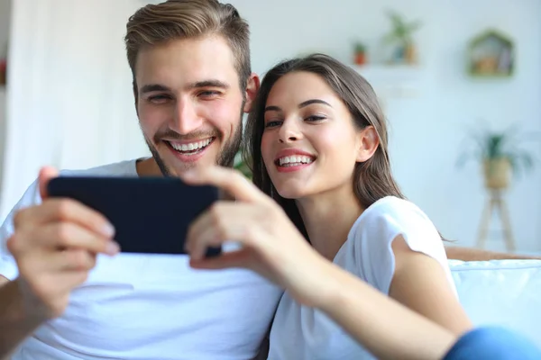 Молода пара дивиться онлайн-контент в смартфоні, сидячи на дивані вдома у вітальні . — стокове фото