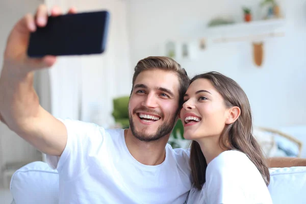 Pareja joven tomando una selfie en el sofá en casa en la sala de estar . —  Fotos de Stock