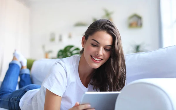 Hermosa mujer joven usando tableta sentada en el sofá en casa en la sala de estar. — Foto de Stock