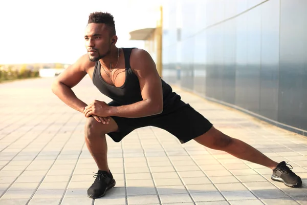 Hombre africano con ropa deportiva calentándose al aire libre, al atardecer o al amanecer . — Foto de Stock