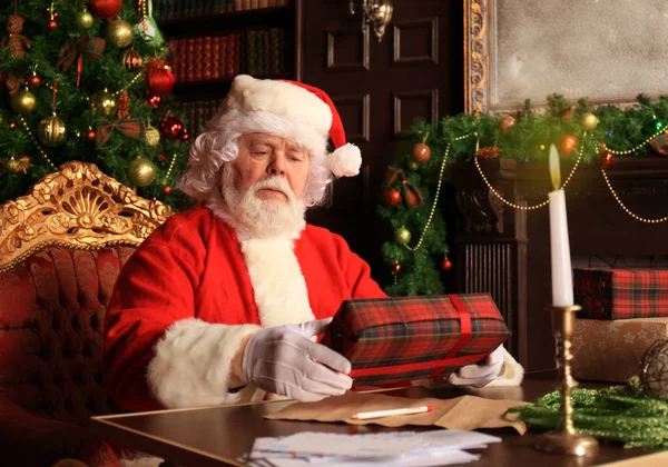 Retrato de Papai Noel feliz sentado em seu quarto em casa perto da árvore de Natal com caixa de presente. — Fotografia de Stock