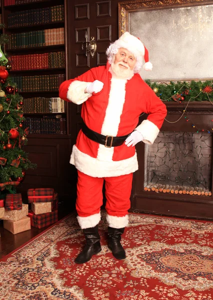 Papai Noel tradicional em pé junto à lareira e árvore de Natal em uma sala. — Fotografia de Stock