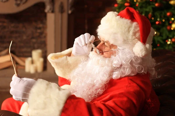 Portrait du Père Noël heureux assis dans sa chambre à la maison près de l'arbre de Noël et lisant la lettre de Noël ou la liste de souhaits. — Photo