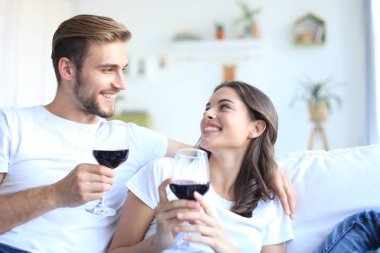 Genç bir çift oturma odasında bir bardak kırmızı şarap içiyor..