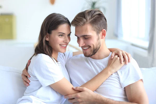 Young loving couple on sofa at home watching tv and laughing.