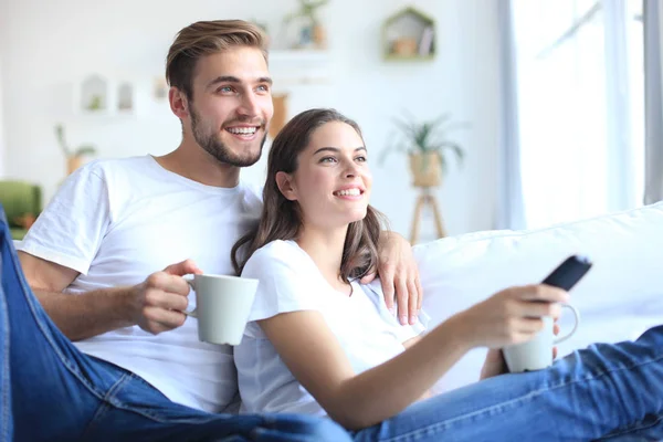 Joven pareja amorosa en el sofá en casa viendo la televisión y riendo. — Foto de Stock