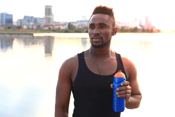 Hombre africano en ropa deportiva ejercicio de agua potable en la playa retrato al aire libre, al atardecer o al amanecer . —  Fotos de Stock