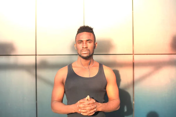 Afrikanska mannen i sportkläder tittar kameran och hålla händer knäppta medan stående utomhus, vid solnedgång, soluppgång. — Stockfoto
