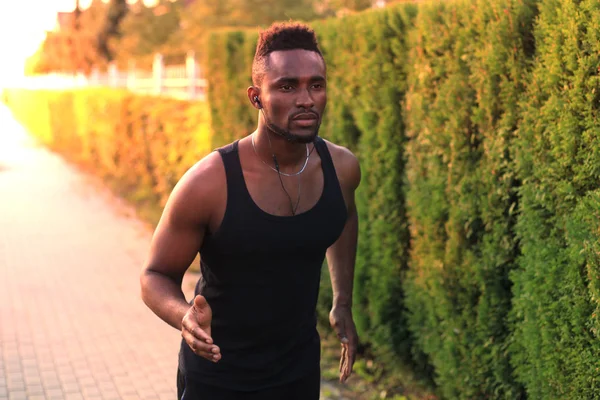 Afrikaanse man in de sport kleding lopen terwijl het uitoefenen buiten, bij zonsondergang of zonsopgang. Loper. — Stockfoto