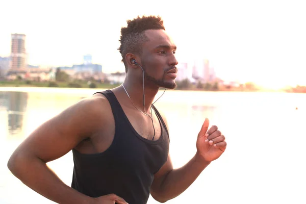 Hombre africano con ropa deportiva corriendo mientras hace ejercicio, en el retrato al aire libre de la playa, al atardecer o al amanecer. Corredor . —  Fotos de Stock