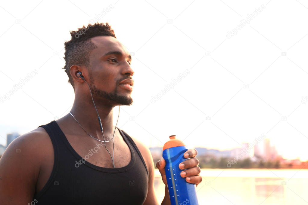 African man in sports clothing drinking water exercise in beach outdoor portrait, at sunset or sunrise.
