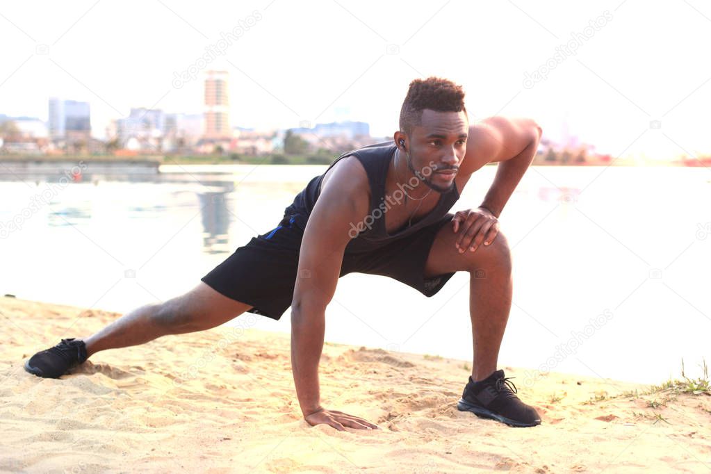 African man in sports clothing warming up, in beach outdoor portrait, at sunset or sunrise.