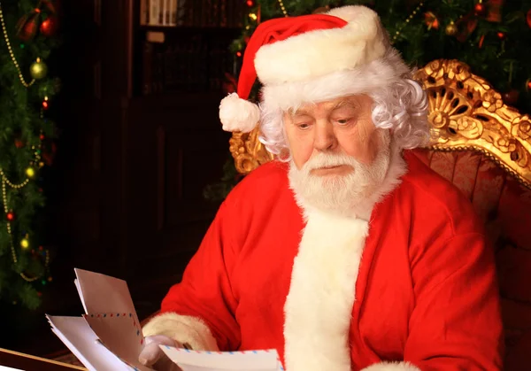 Papai Noel sentado na árvore de Natal, segurando cartas de Natal e tendo um descanso junto à lareira. — Fotografia de Stock