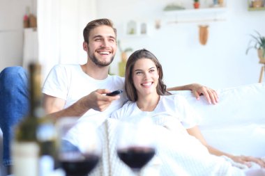 Seven çift kanepe evde genç tv izlerken ve gülüyor, bir kadeh kırmızı şarap içmek.