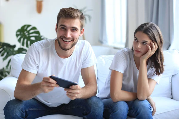 Hombre jugando videojuegos mientras su novia se enoja con él en su sala de estar . — Foto de Stock