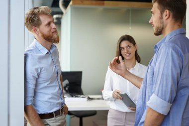 Group of young modern people in smart casual wear having a brainstorm meeting while standing in the creative office. clipart