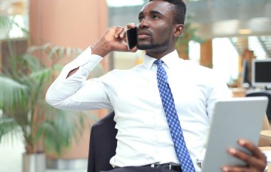 Tablet bilgisayar kullanarak ve telefonda konuşurken başarılı bir Afrikalı-Amerikalı girişimci.