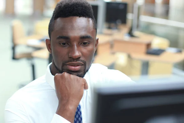 Retrato de um empresário afro-americano bem-sucedido sentado à mesa com computador no escritório . — Fotografia de Stock