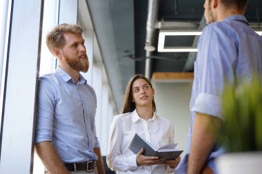 Group of young modern people in smart casual wear having a brainstorm meeting while standing in the creative office. clipart