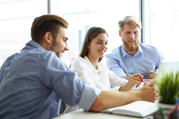 Groupe de jeunes gens modernes en tenue décontractée intelligente pointant vers un ordinateur portable et souriant tout en étant assis dans le bureau . — Photo