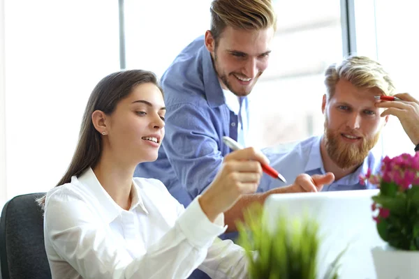 Gruppe junger moderner Menschen in schicker Freizeitkleidung zeigt auf Laptop und lächelt im Büro. — Stockfoto