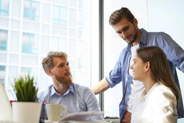 Jóvenes colegas en ropa casual inteligente trabajando mientras pasan tiempo en la oficina . — Foto de Stock