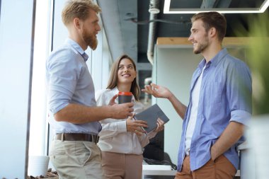 Group of young modern people in smart casual wear having a brainstorm meeting while standing in the creative office. clipart