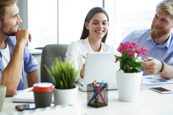 Gruppo di giovani moderni in abbigliamento casual intelligente che puntano al laptop e sorridono mentre sono seduti in ufficio . — Foto Stock