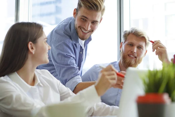 Grupp unga moderna människor i vårdad bära pekar på laptop och ler medan du sitter på kontoret. — Stockfoto